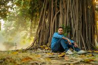 A Man Sitting on the Ground Near a Banyan Tree