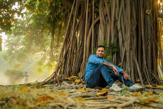 A Man Sitting on the Ground Near a Banyan Tree