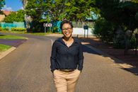 Confident woman walking on a sunny street, smiling with hands in pockets.