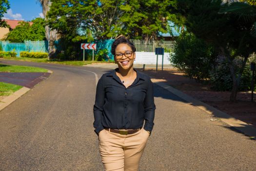 Confident woman walking on a sunny street, smiling with hands in pockets.