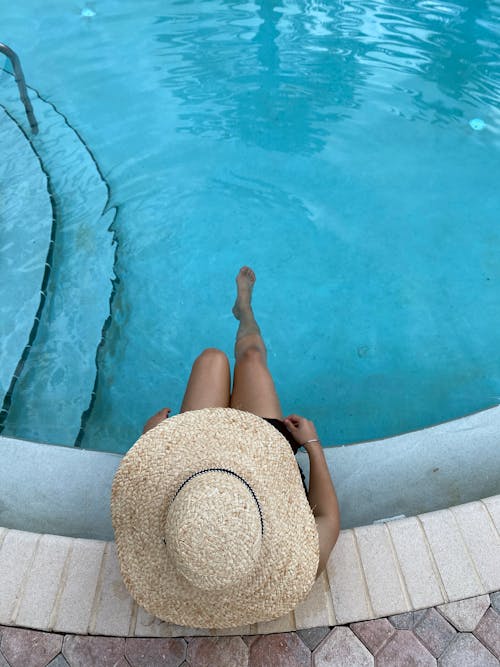 A Person Wearing a Straw Hat Sitting at the Poolside