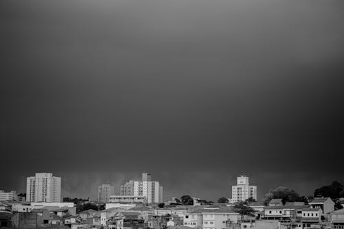 Free Black and white of gray cloudless sky over tall multistorey buildings and typical aged residential buildings on street in city Stock Photo