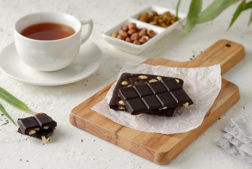 Free Indulgent chocolate bars with nuts paired with a cup of tea on a wooden board. Stock Photo