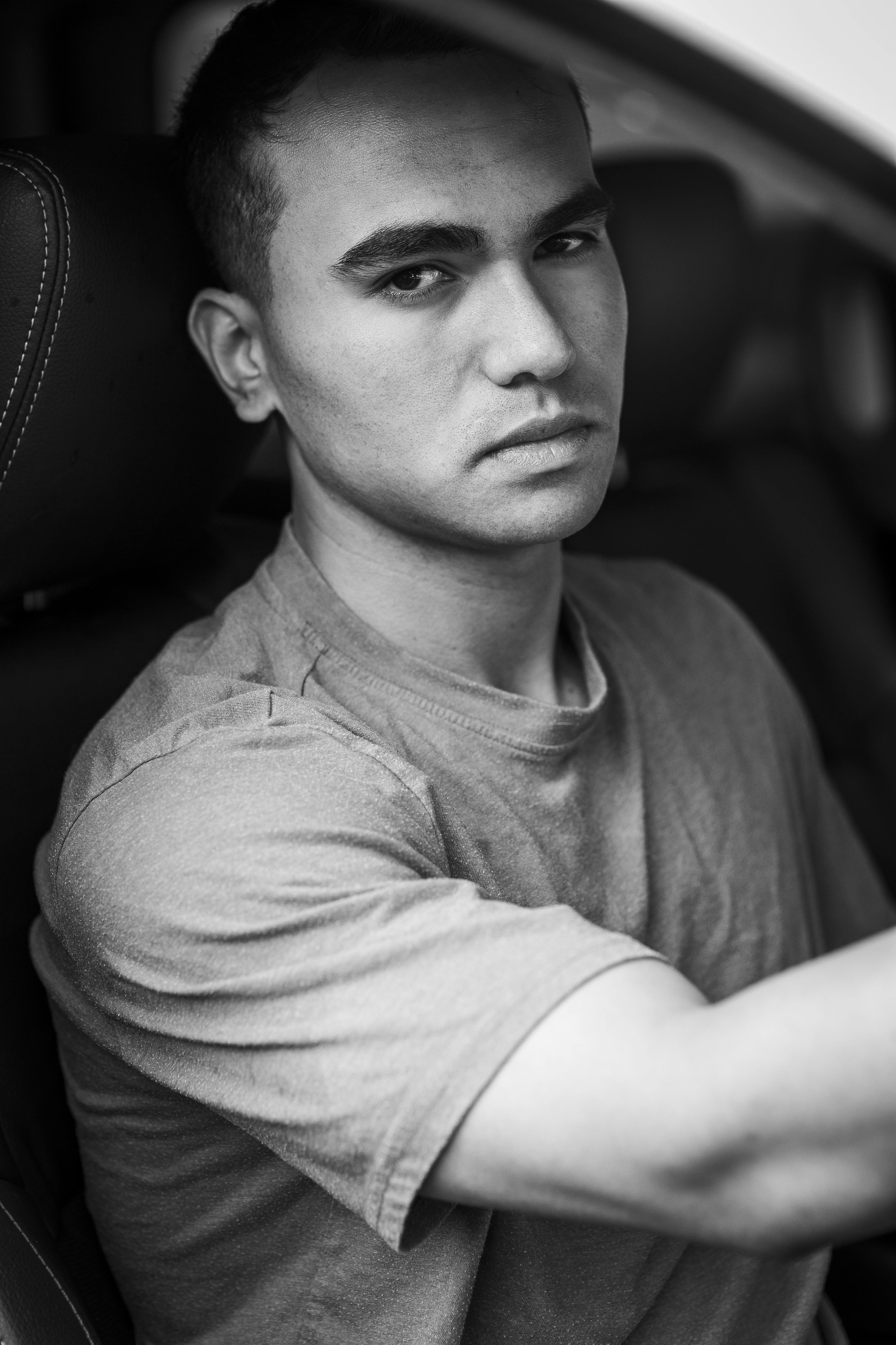 Black and white portrait of a man sitting in a car, staring thoughtfully.
