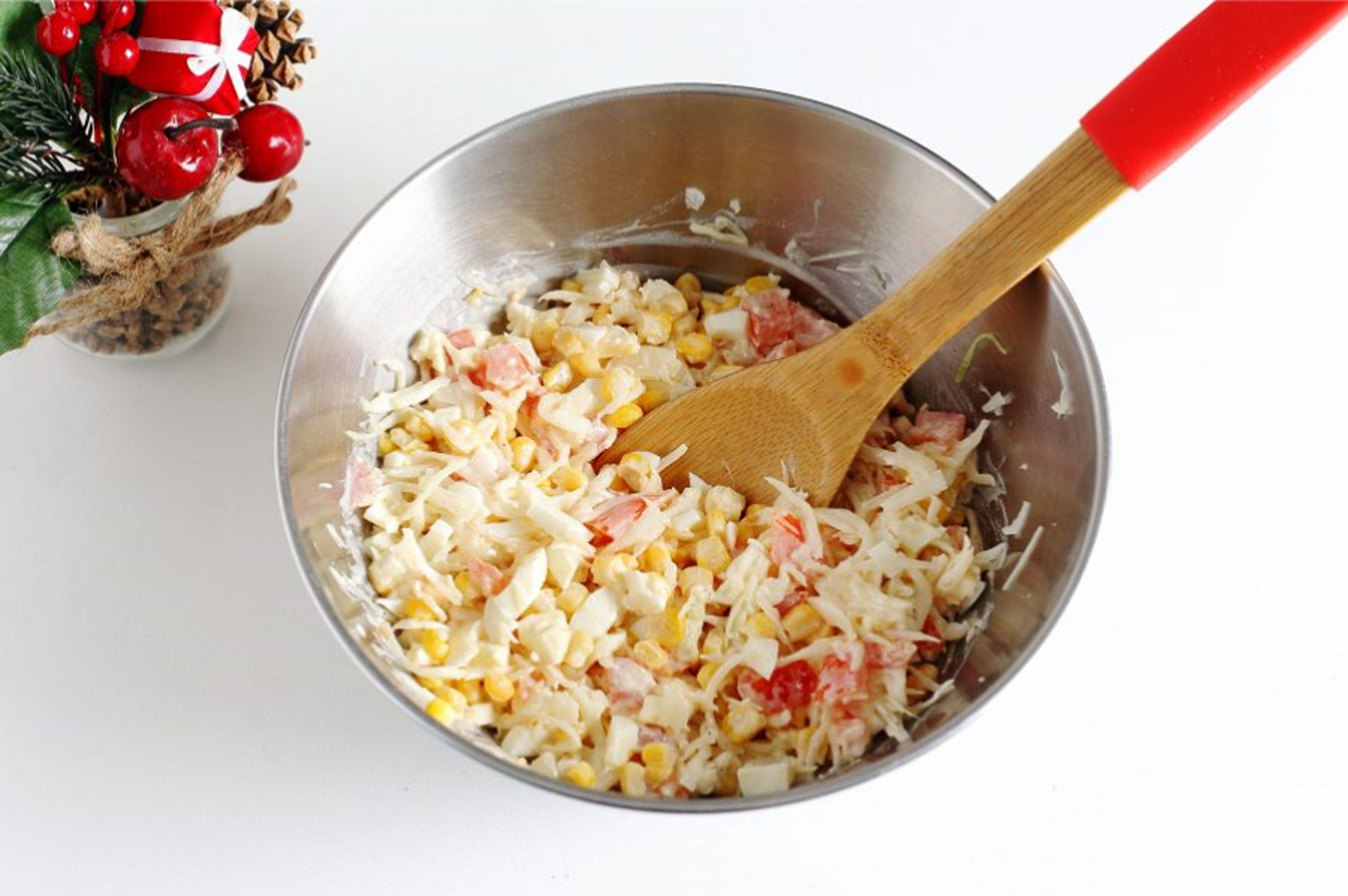 Homemade salad of corn, cabbage, and tomatoes in a stainless steel bowl with holiday decor.