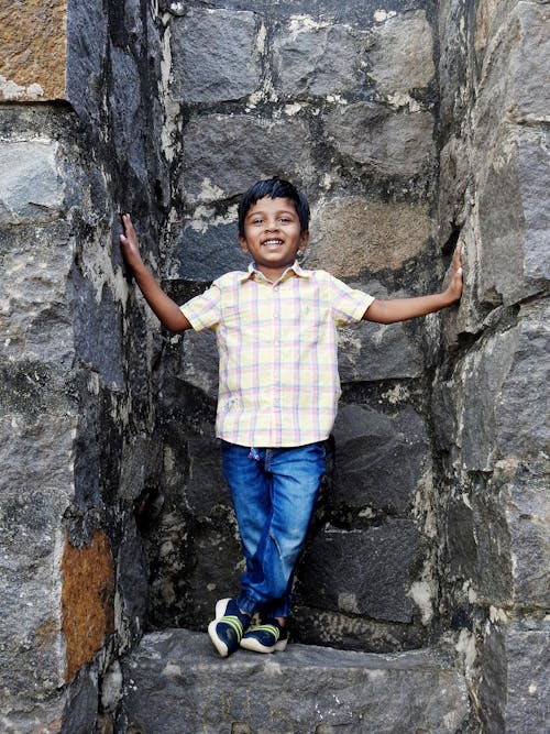 Boy  in Plaid Button Up Shirt and Blue Denim Jeans Standing Between Stone Walls