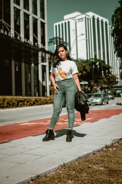 Free Asian woman in casual wear and black boots posing confidently on a city sidewalk. Stock Photo