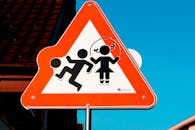 三角形路标描绘儿童玩耍的场景，在明亮的蓝天下强调安全性