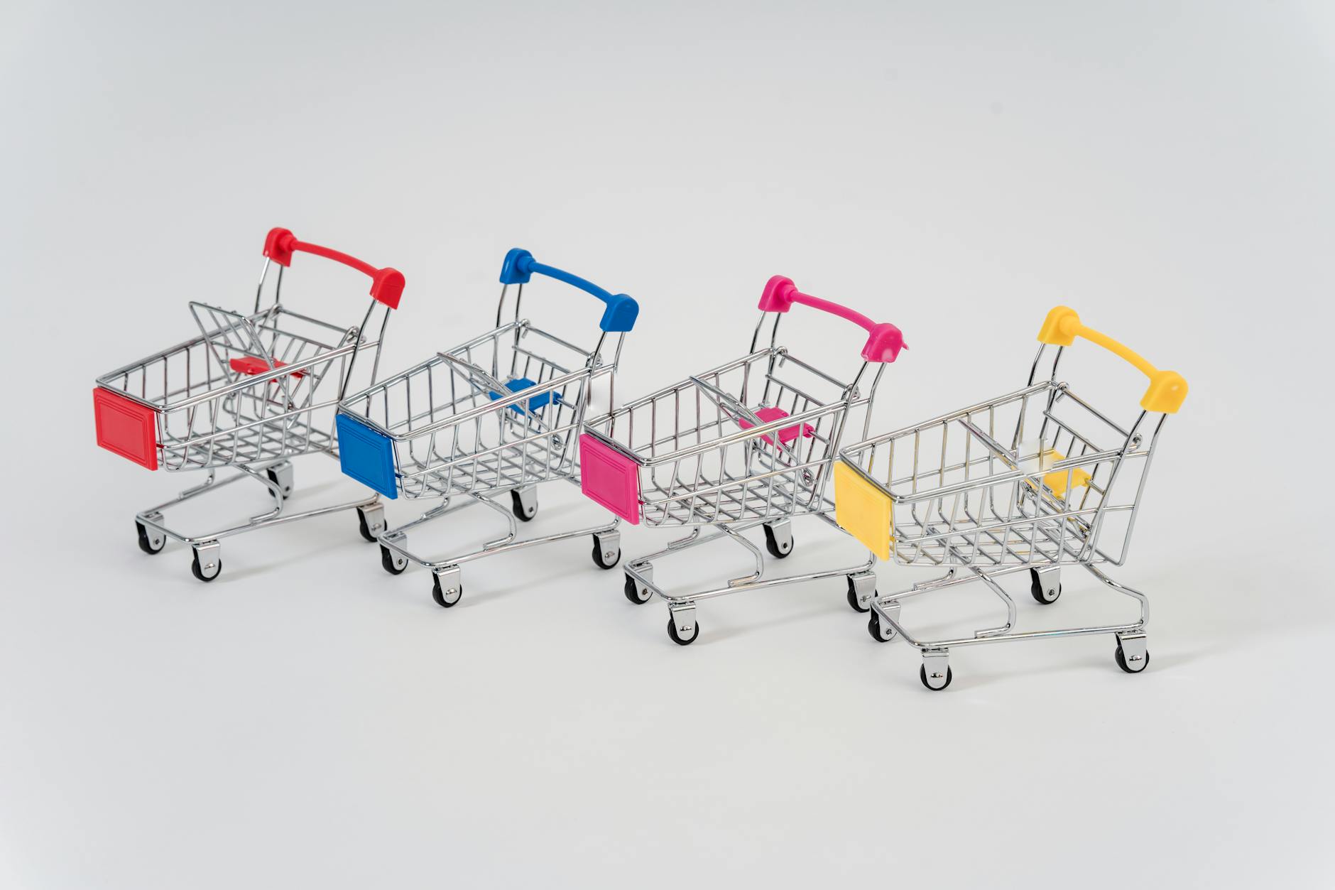 Four miniature shopping carts with colorful handles aligned on a white background for conceptual business imagery.