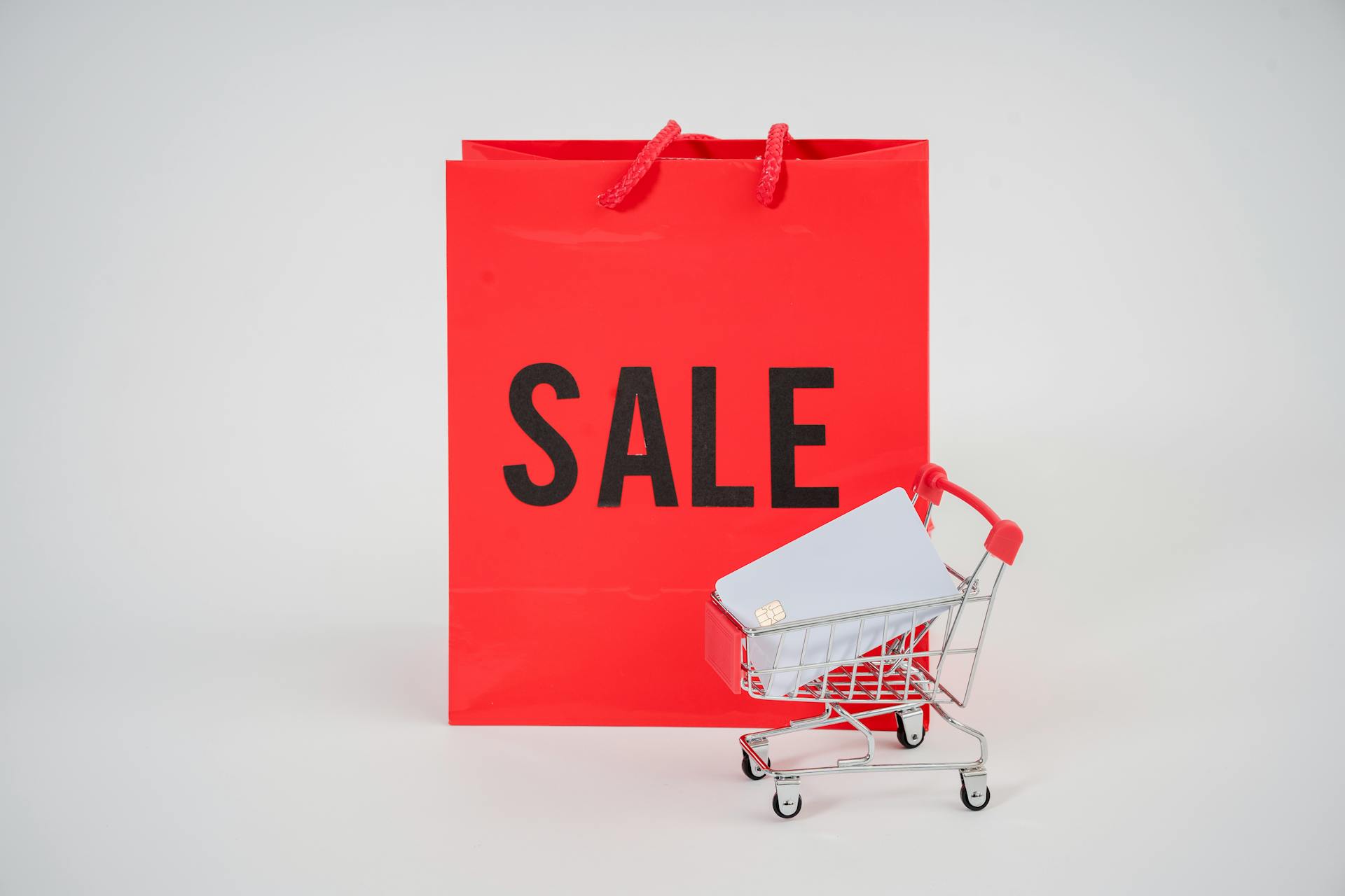 Photo Of Mini Push Cart With Bank Card Beside Red Paper Bag