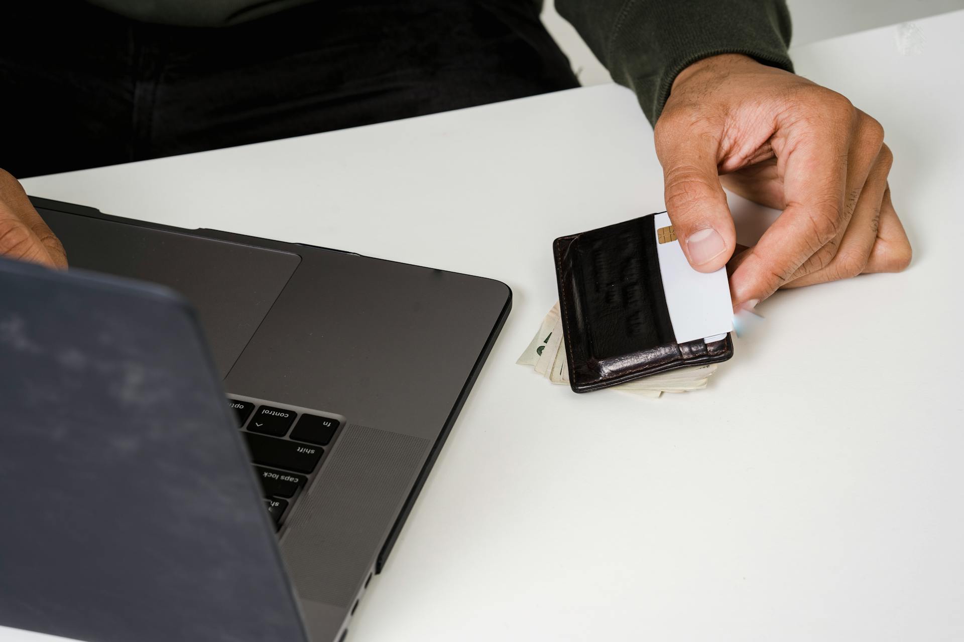 Close-up of a hand holding a credit card near a laptop for an online transaction.