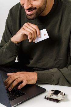 一名男子正用笔记本电脑和信用卡在线购物，旁边放着现金和钱包