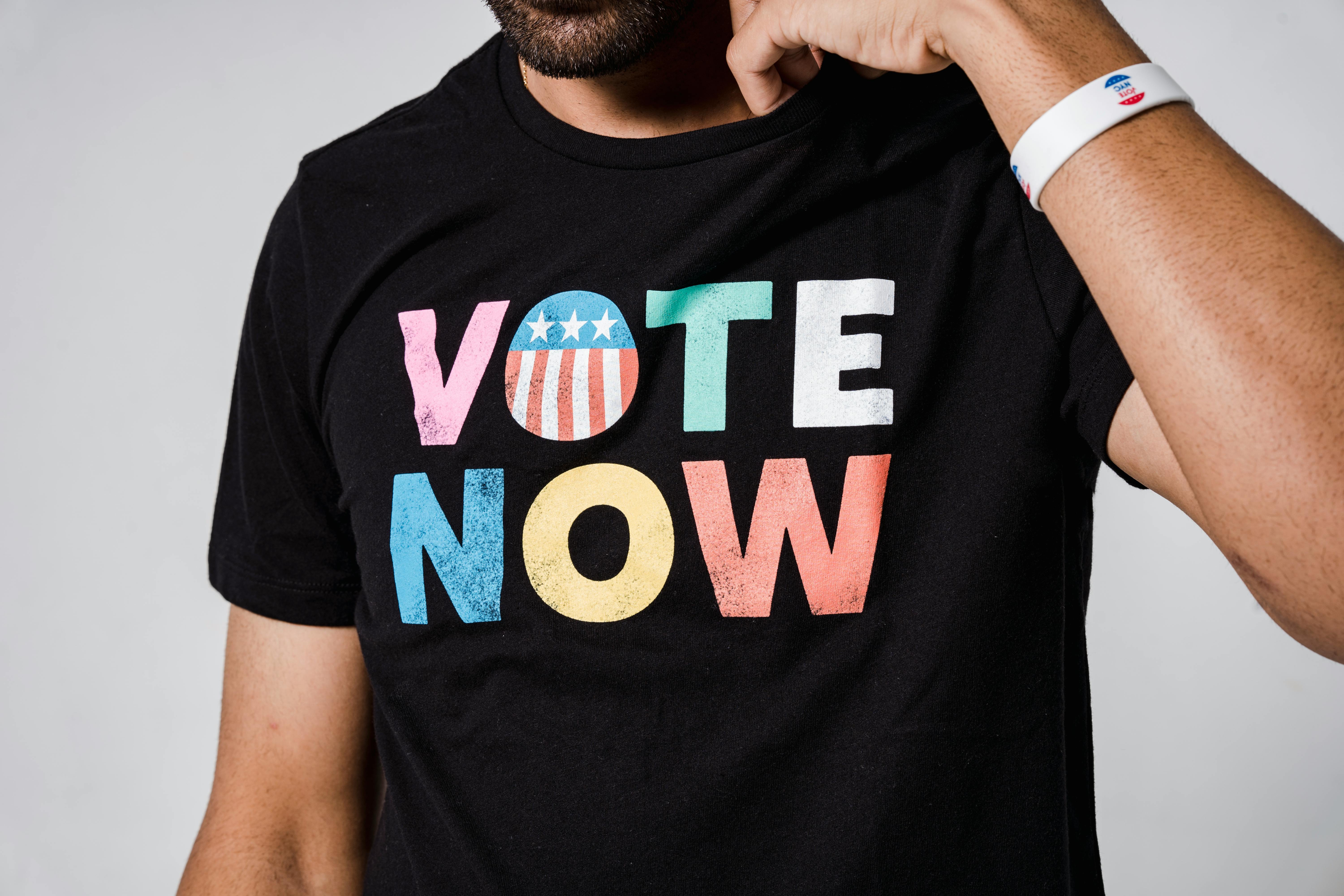 A close-up shot of a black t-shirt with colorful Vote Now text, promoting voting awareness.