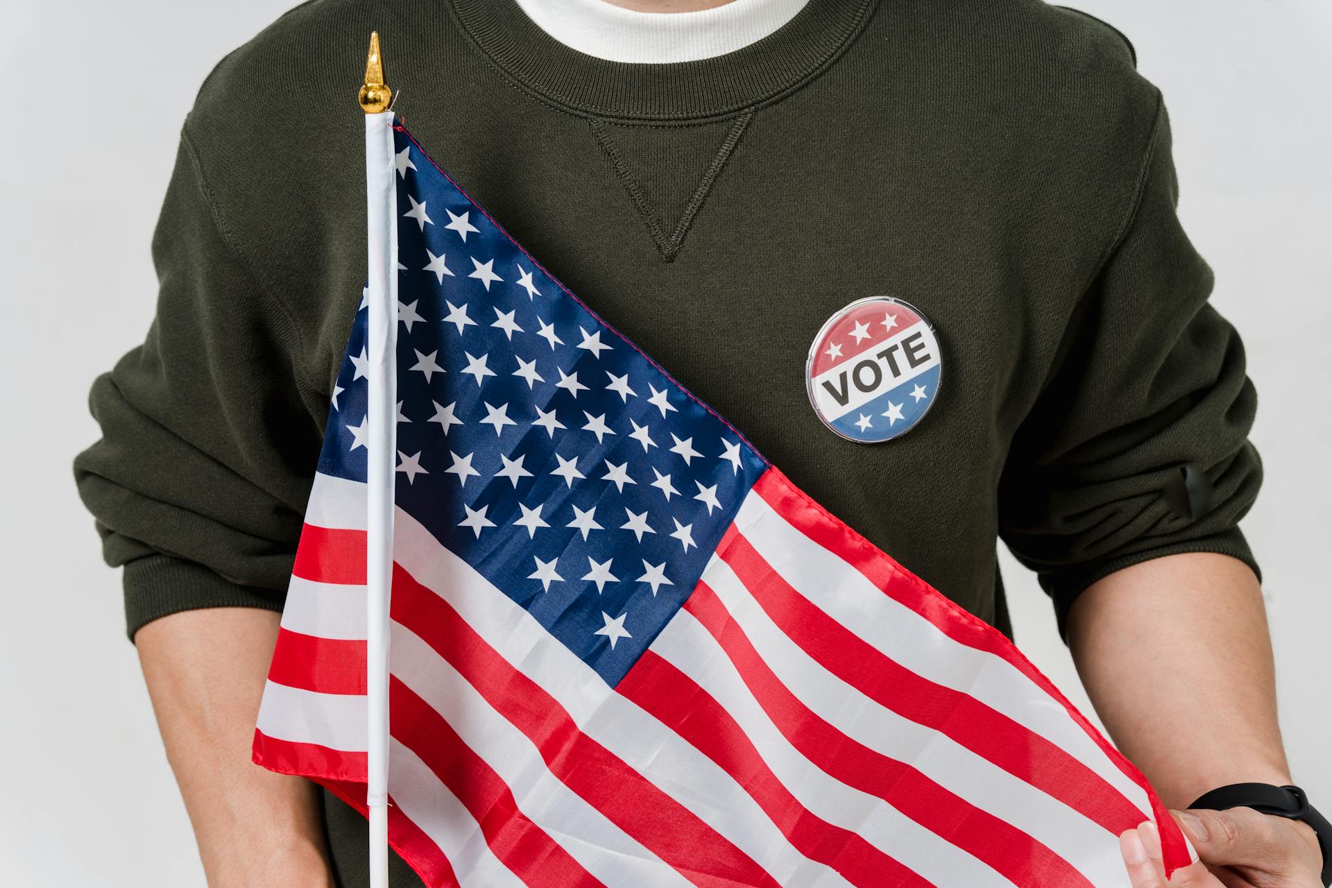 Close-up of a Man Holding the Flag of the United States and a Pin with a Word "Vote"