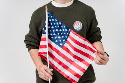 Close-up of a Man Holding the Flag of the United States and a Pin with a Word "Vote"