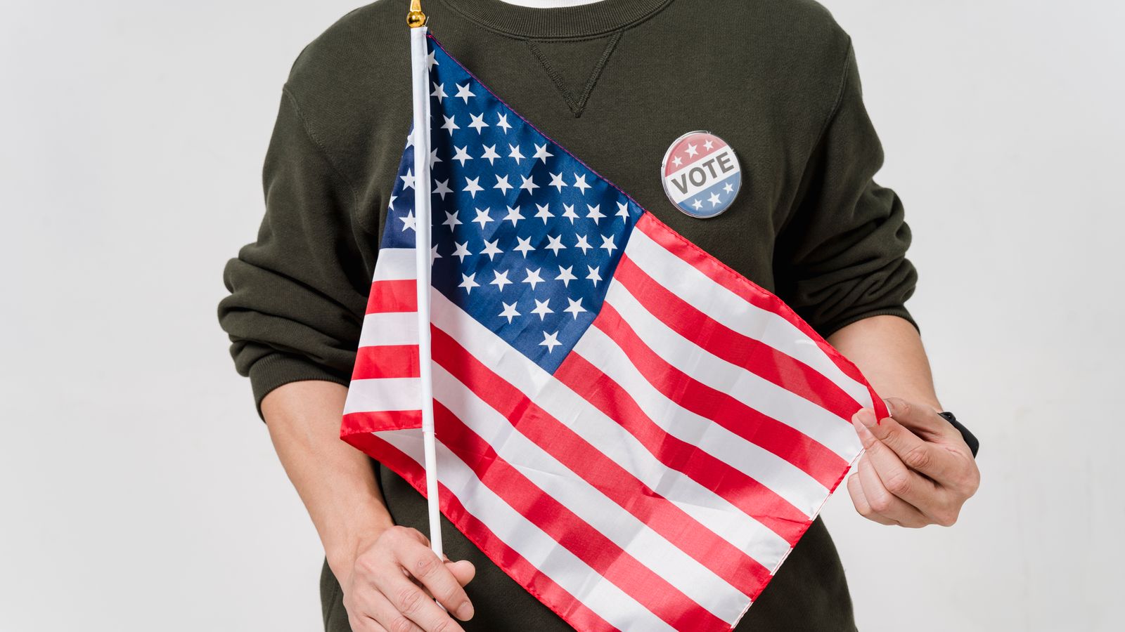 A man holding a USA flag and wearing a vote badge, symbolizing patriotism and democratic participation.