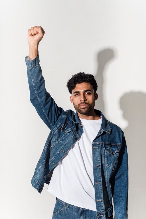 Free Portrait of a confident man in a denim jacket raising his fist, symbolizing empowerment. Stock Photo