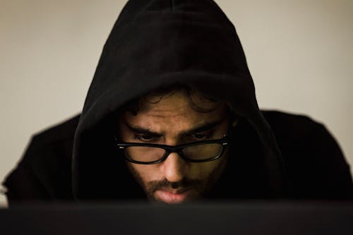 Concentrated hacker in hood using laptop