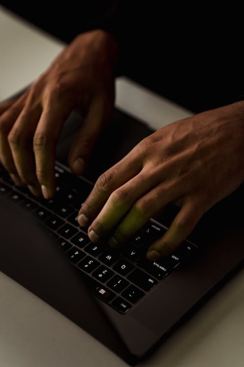 暗闇の中でノートパソコンのキーボードで入力する顔のない人をトリミングします