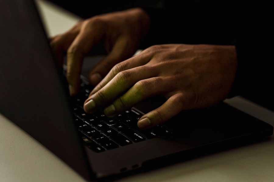 Crop anonymous person working on modern netbook and typing on keypad while surfing internet in dark room