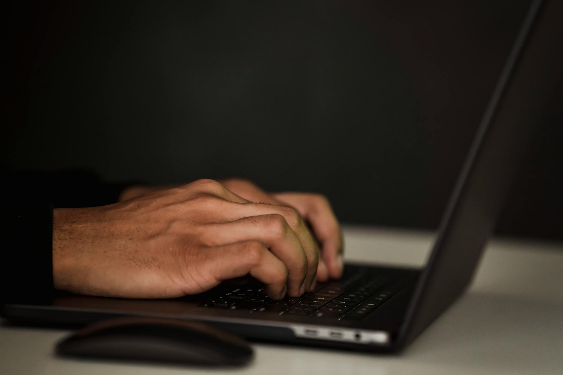 Crop unrecognizable person surfing internet on contemporary netbook and typing on keyboard in dark workspace