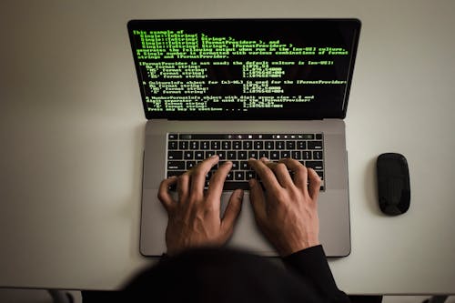 Free From above crop anonymous male programmer in black hoodie working on software code on contemporary netbook and typing on keyboard in workspace Stock Photo