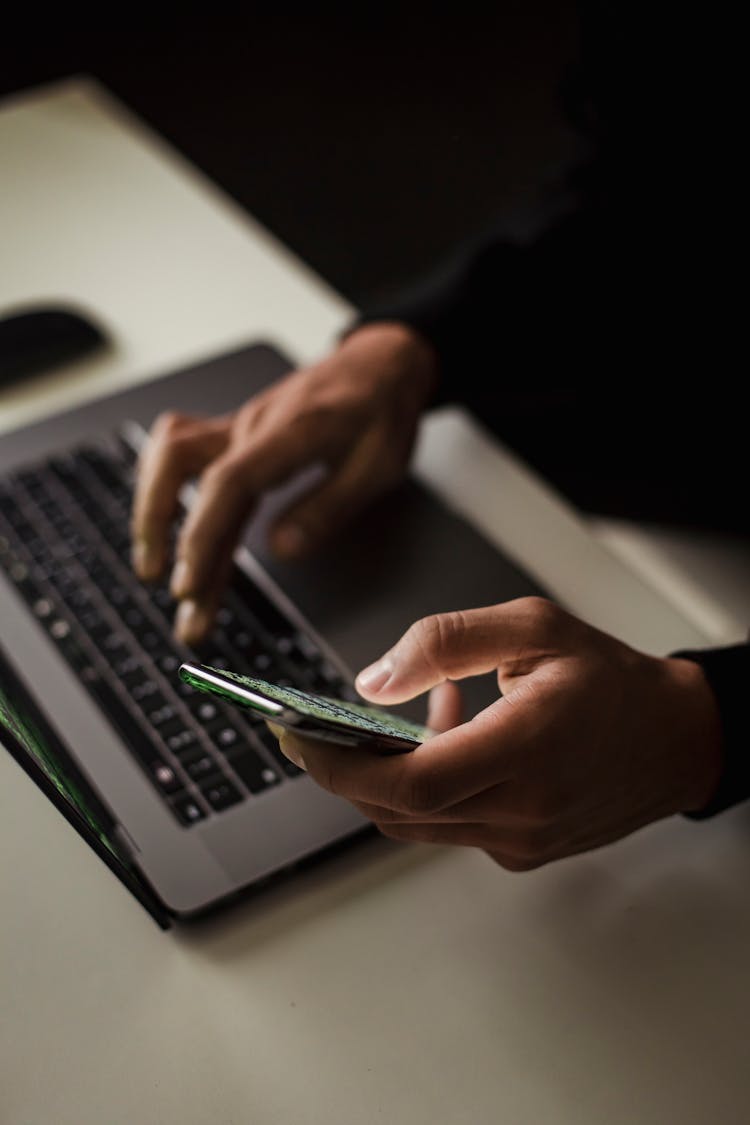 Crop Faceless Person Using Laptop And Smartphone In Darkness