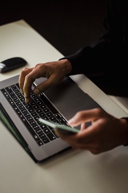 High angle crop male in black clothes browsing contemporary netbook and mobile phone while working in office