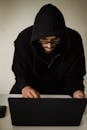 From above concentrated young male hacker in black hoodie browsing dark net on netbook and hacking software in studio