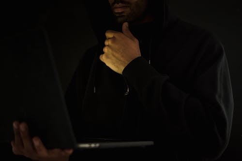 Crop pensive hacker using laptop and touching chin