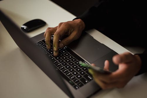 Free Crop faceless man typing on laptop and using smartphone Stock Photo