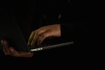 Crop unrecognizable man typing on laptop in obscurity