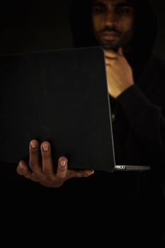 一名戴着黑色兜帽的男性黑客正对着上网本沉思，他一边看视频，一边摸着下巴