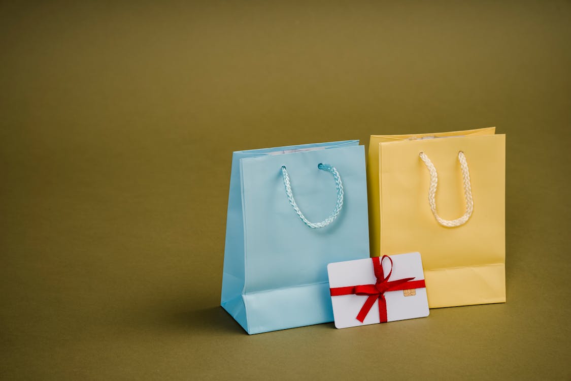 Free Collection of bright present paper bags with natural handles near gift card with ribbon Stock Photo