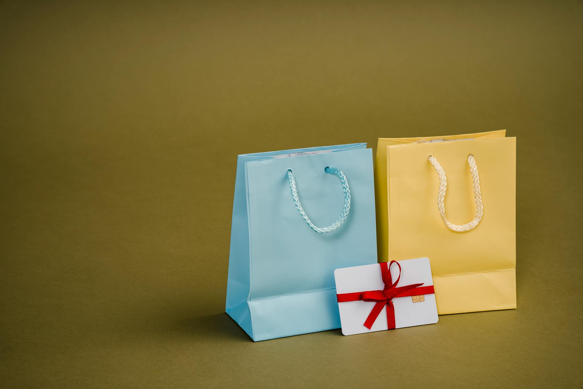 Collection of bright present paper bags with natural handles near gift card with ribbon