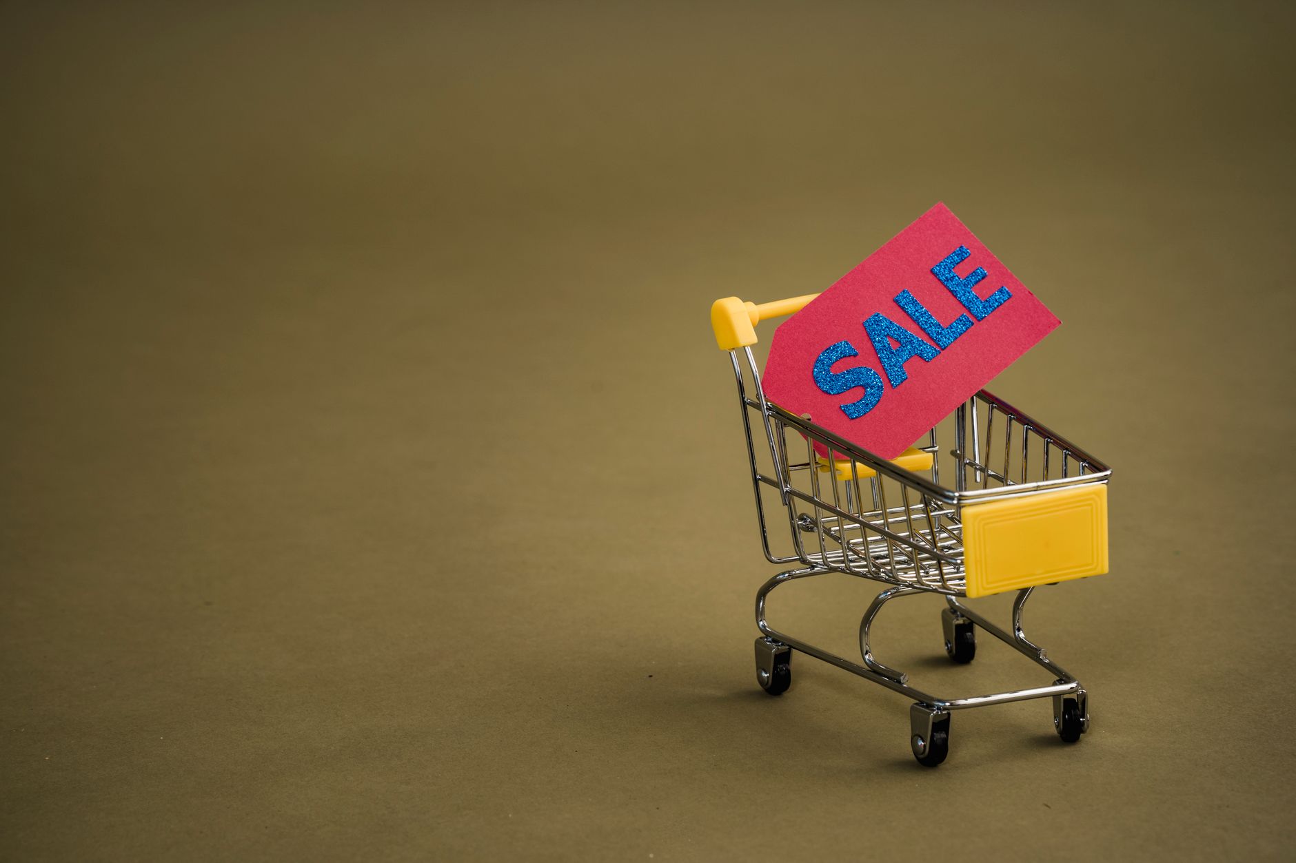 A miniature shopping cart with a bright red 'SALE' tag on a neutral brown background. (Photo by Sora Shimazaki on Pexels)