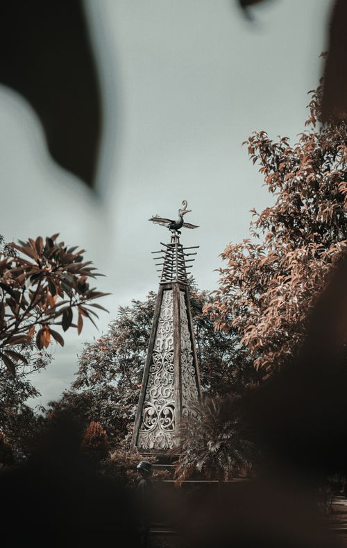 Free A decorative metal structure stands tall amidst abundant trees in a serene outdoor setting. Stock Photo