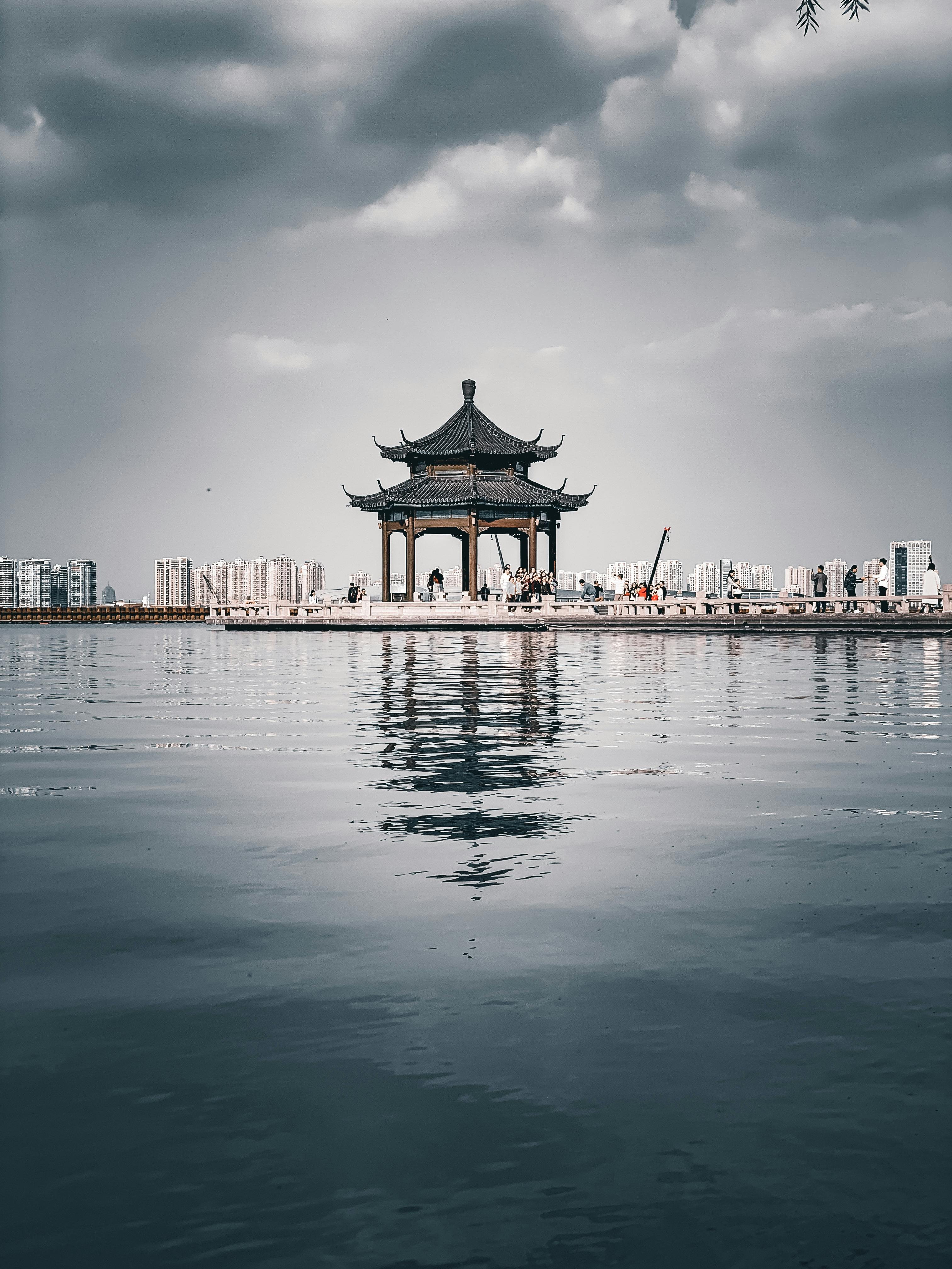 Traditional Chinese gazebo reflecting on a lake under a cloudy sky in Suzhou, China.