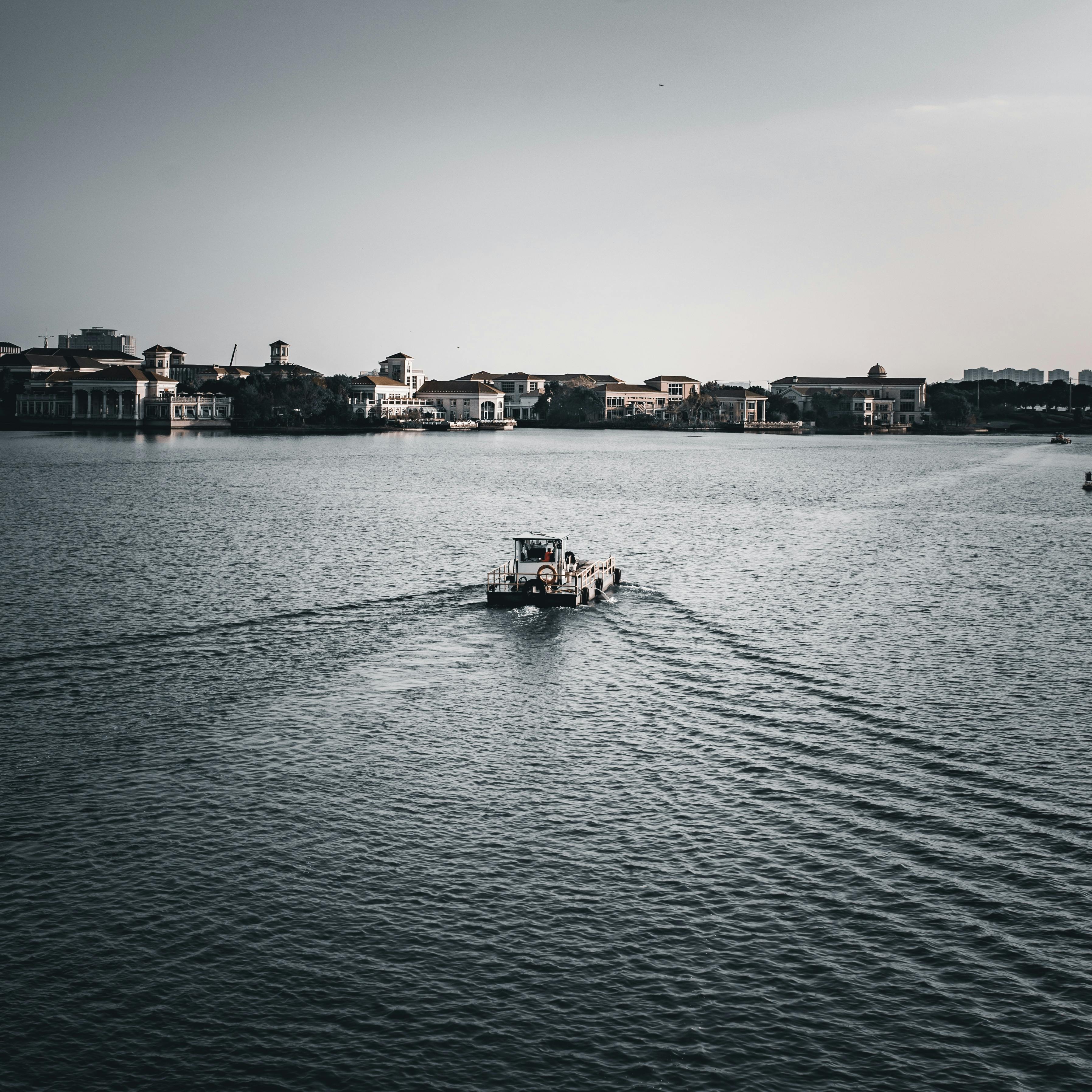 Free Small boat navigating a calm waterfront with buildings in the background. Stock Photo