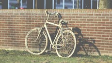 一辆锈迹斑斑的旧自行车靠在砖墙上，在阳光下投下阴影