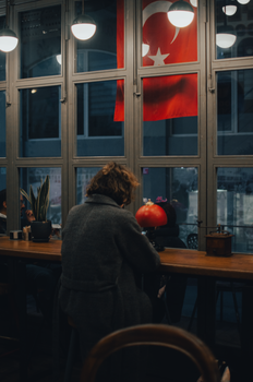 Back view of unrecognizable female customer sitting at wooden counter near window in bar in evening