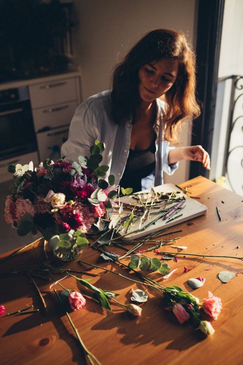 Free A woman arranging a flower bouquet in a sunlit room, creating a floral masterpiece. Stock Photo