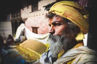 Side view contemplative senior Indian male with long gray beard wearing yellow turban standing on street and looking away pensively