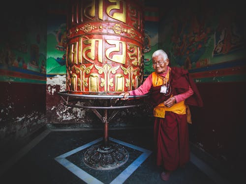 Mature monk walking around prayer wheel in temple