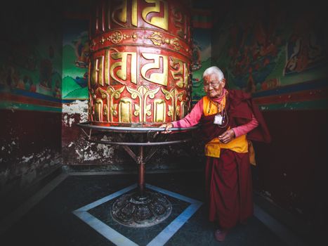 一位安详的老和尚站在寺庙里色彩缤纷的转经轮旁