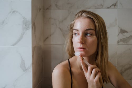 Woman in Black Spaghetti Strap Top Using Jade Roller On Face