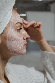 Close-up of a woman applying a clay mask for skincare and relaxation.