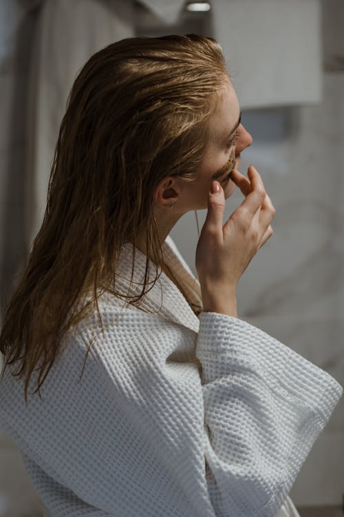 Free Young woman in bathrobe applying cosmetic mask on face Stock Photo