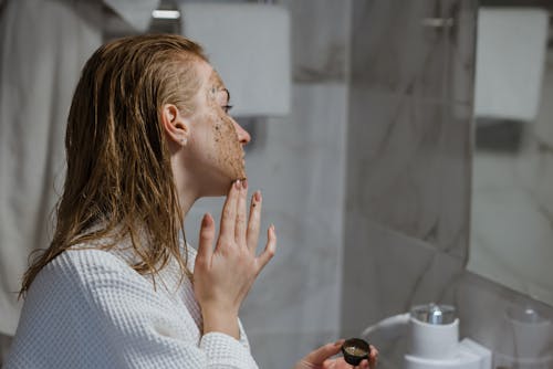 Free Woman Applying Coffee Scrub On Face In Front Of A Mirror Stock Photo