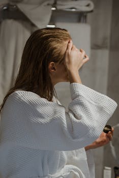 Side view of a woman applying a facial mask in a bathroom setting.